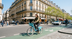 Cycliste sur un Vélib électrique dans une piste cyclable parisienne devant des immeubles haussmanniens au printemps