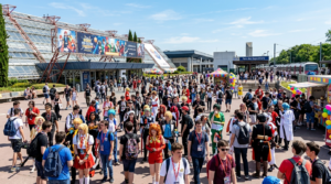 Visiteurs en cosplay et habits d'été arrivant à l'entrée du Parc des Expositions Paris-Nord Villepinte pour Japan Expo 2026, avec la gare RER visible en arrière-plan