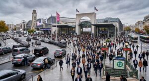 Entrée principale de Paris Expo Porte de Versailles lors du Mondial de l'Auto 2026, avec des visiteurs arrivant, la station de métro ligne 12 visible et des taxis en zone de dépose