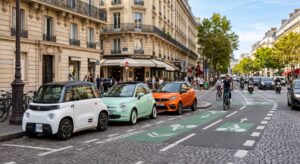 Trois voitures sans permis électriques de styles différents garées côte à côte sur une rue parisienne ensoleillée avec une piste cyclable visible