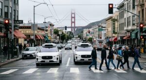Deux robotaxis Waymo autonomes à un feu rouge à San Francisco, capteurs visibles sur le toit, avec le Golden Gate Bridge en arrière-plan dans la brume californienne